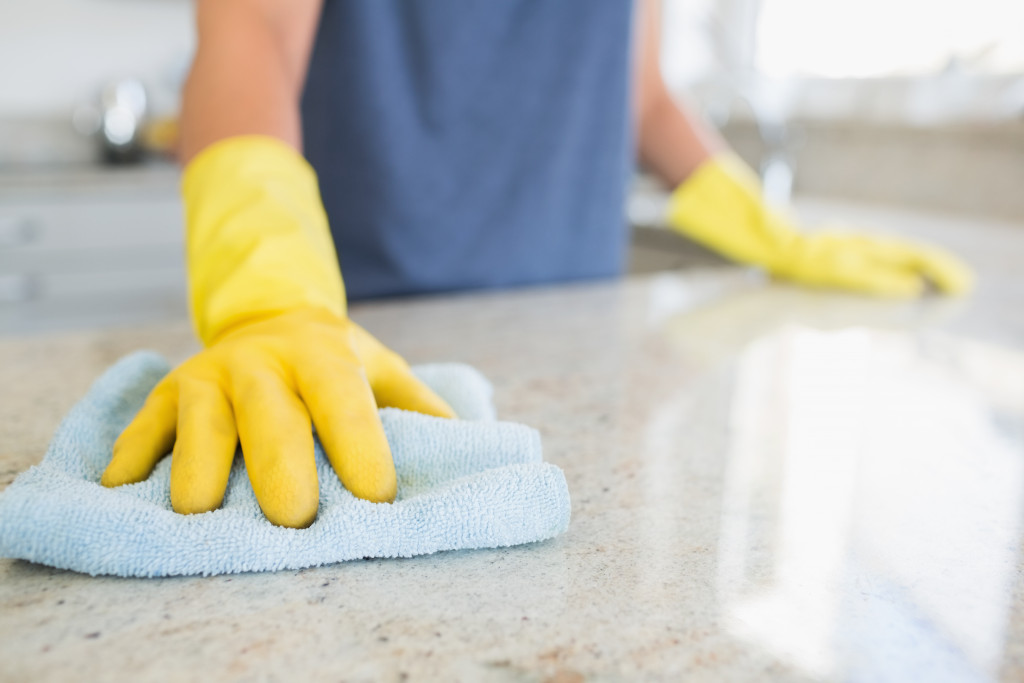 A person wearing yellow rubber glove wiping a kitchen countertop