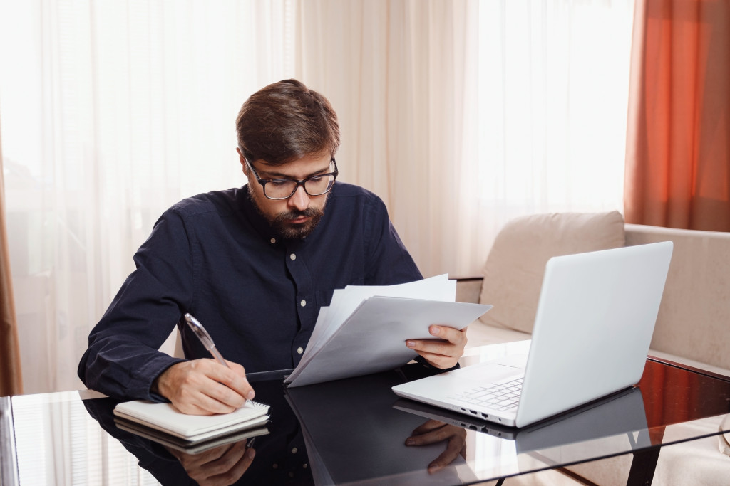 Young entrepreneur wearing glasses working from home using a laptop and documents.