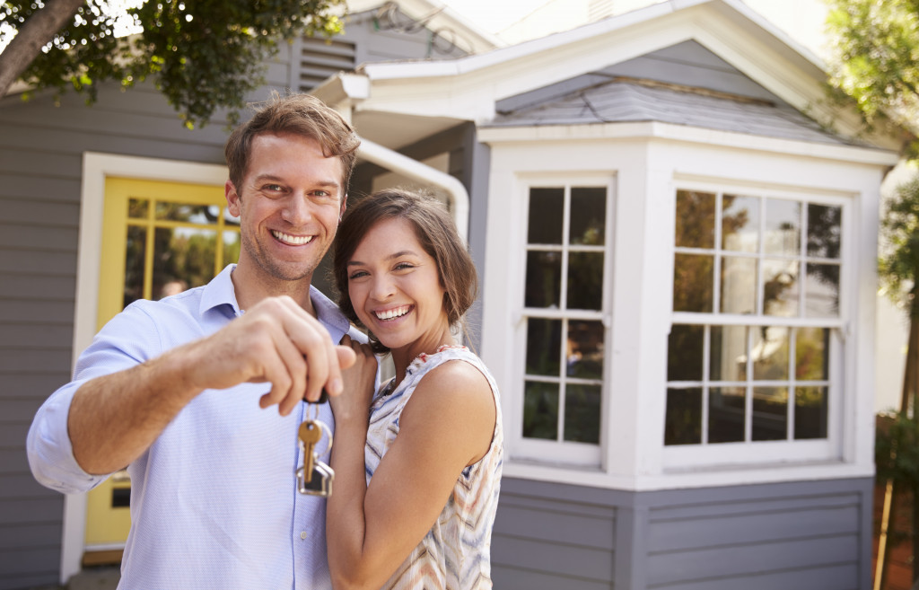 A couple smiling and showing off a set of keys in front of a clean house